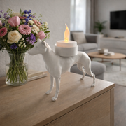 Witte waxinelichthouder windhond op houten kast naast bos bloemen in moderne woonkamer.